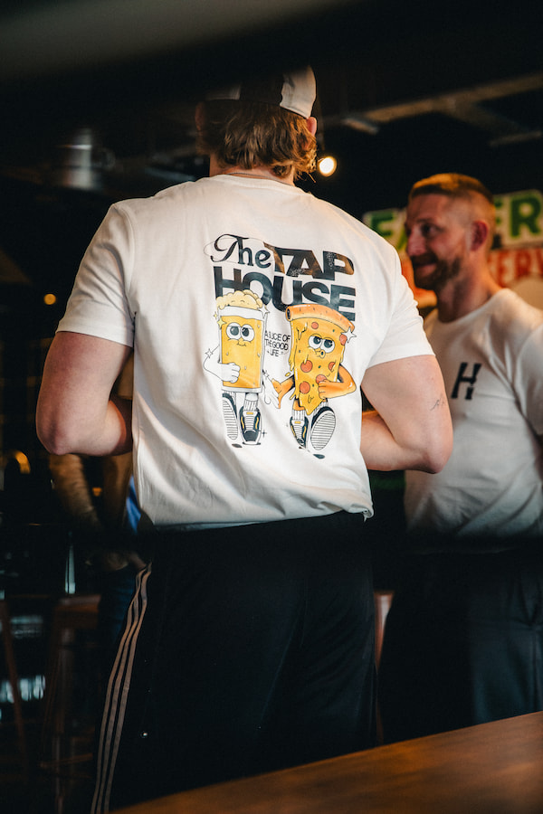 Two people talking wearing The Tap House Manchester t-shirt with a print on the back.